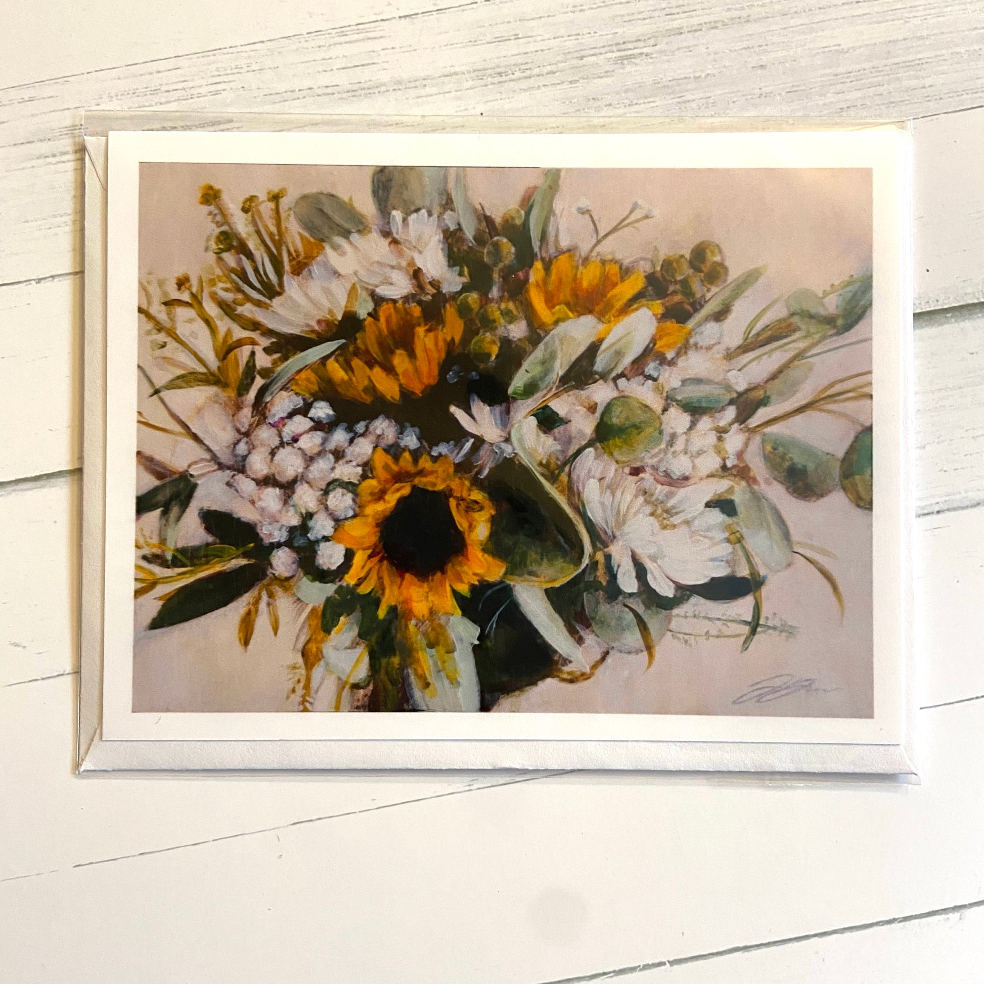 A folded landscape-style greeting card with a painting on the front of a floral bouquet, featuring sunflowers with greenery and white blooms on a beige background. 