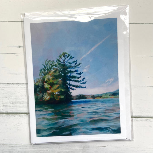 A folded white greeting card with an image of my painting, Surface Level, which depicts a view from Webster Lake in Franklin, NH. The focus is a small peninsula of trees including a prominent pine tree, jutting out into the calm blue water and sky. 