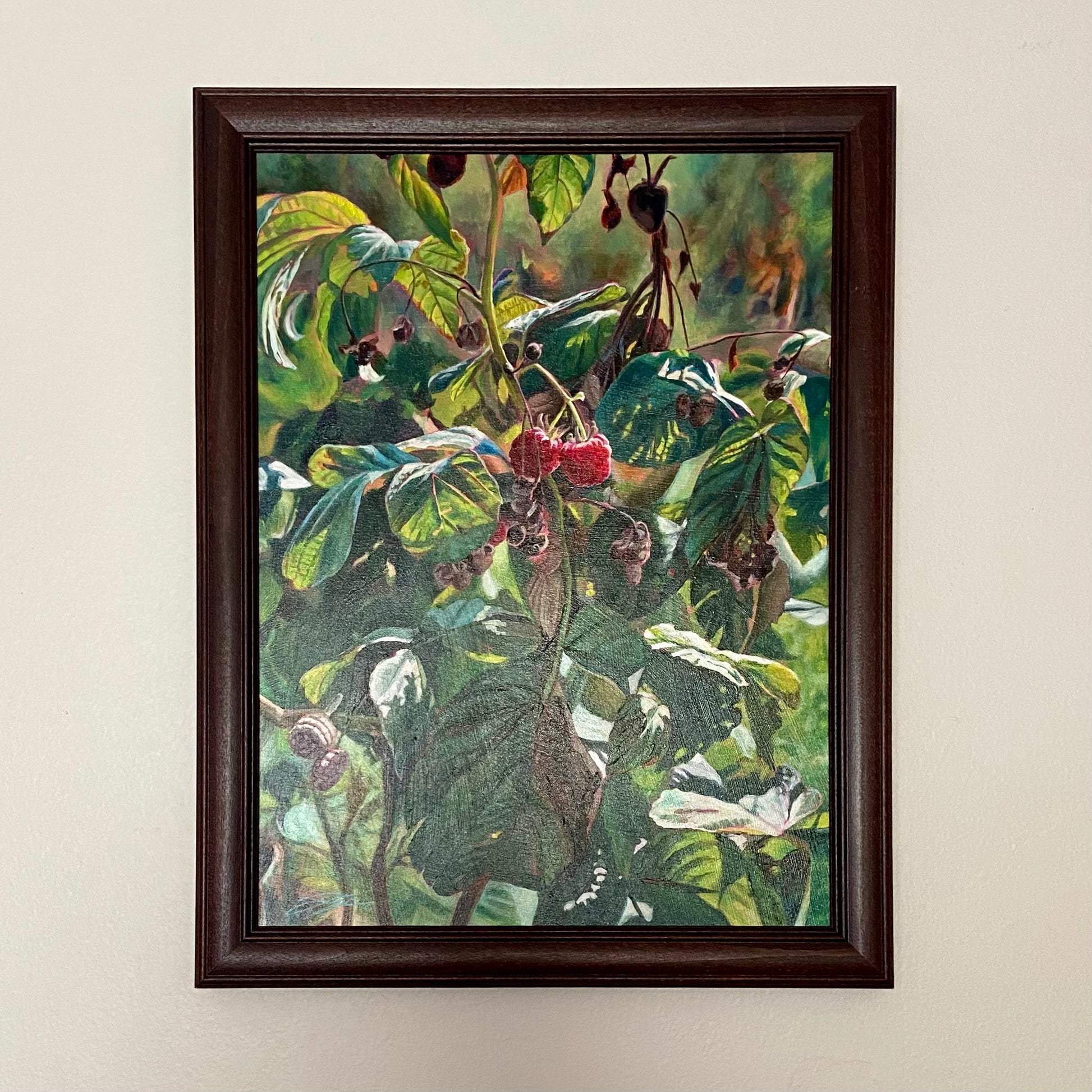 My acrylic painting of a realistic raspberry plant, titled “Two Truths”, hangs on an off-white wall in a dark brown wood frame.