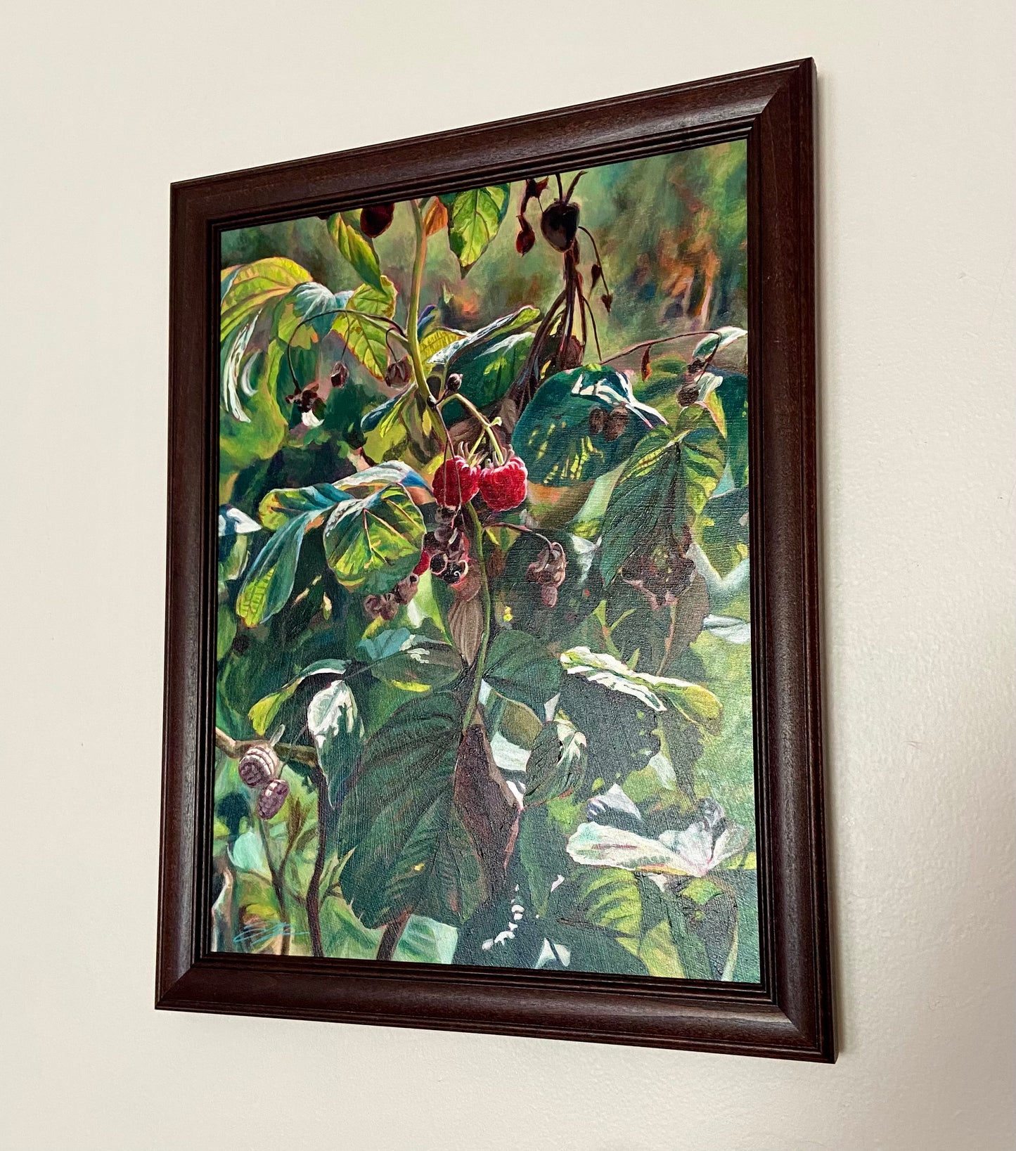 My acrylic painting of a realistic raspberry plant, titled “Two Truths”, hangs on an off-white wall in a brown wood frame.