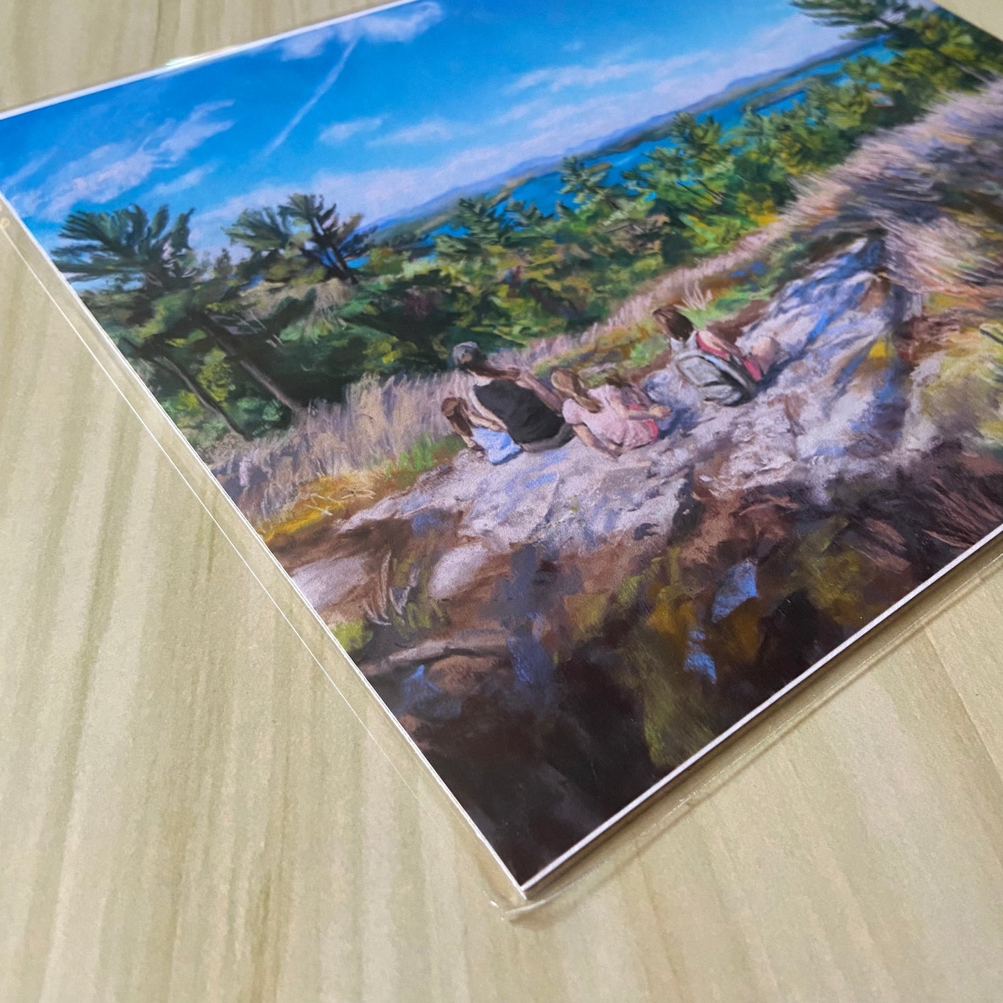 An angled detail view of the art print. The chalky texture of the soft pastel is shown here, especially in the grass and rocks of the mountain. The blue lake and sky are bright, smooth blue.