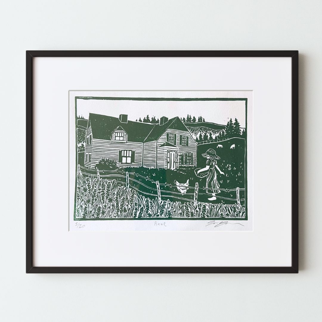 A mockup of a green and white carved relief print (stamp) in a black frame with a white mat. The print shows an old home on a field with animals and fences. A girl in a dress and straw hat carries a basket toward the house.