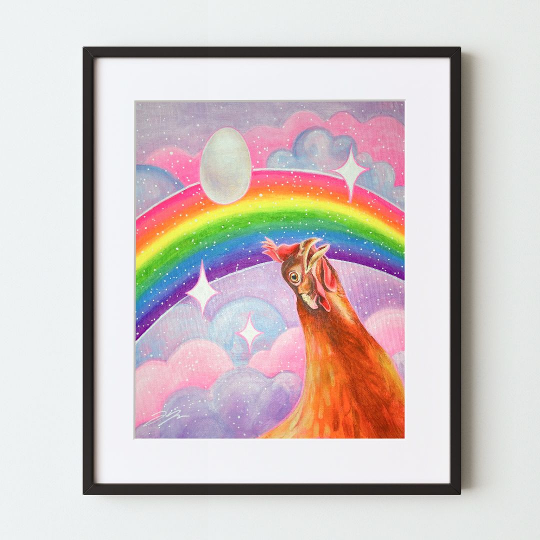 A mockup of an art print in a black frame with a white mat. The artwork depicts an orange chicken at bottom left, looking awed up at a pink-and-purple sky with a rainbow, sparkles, and a floating egg.