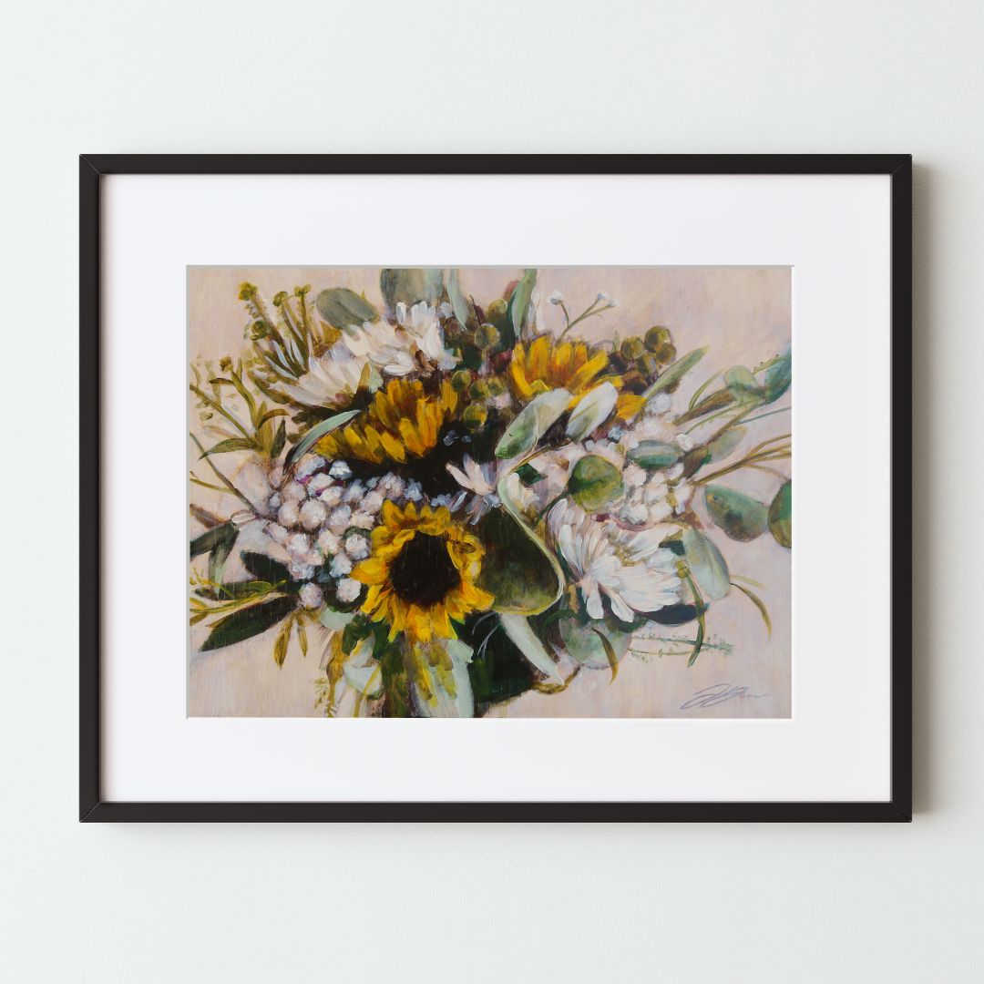 A mockup of a floral art print in a black frame with white mat. The artwork shows a clustered bouquet of sunflowers mixed with other white flowers and greenery, all on a beige background. The artist's signature can be seen at bottom right.